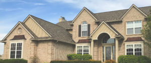 A large suburban house with a beige brick facade, pointed roofs, and arched windows under a clear sky.