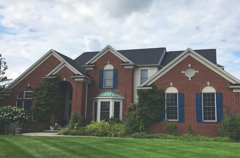 A large brick house with multiple arched windows, a dark roof, and a manicured lawn under a cloudy sky.