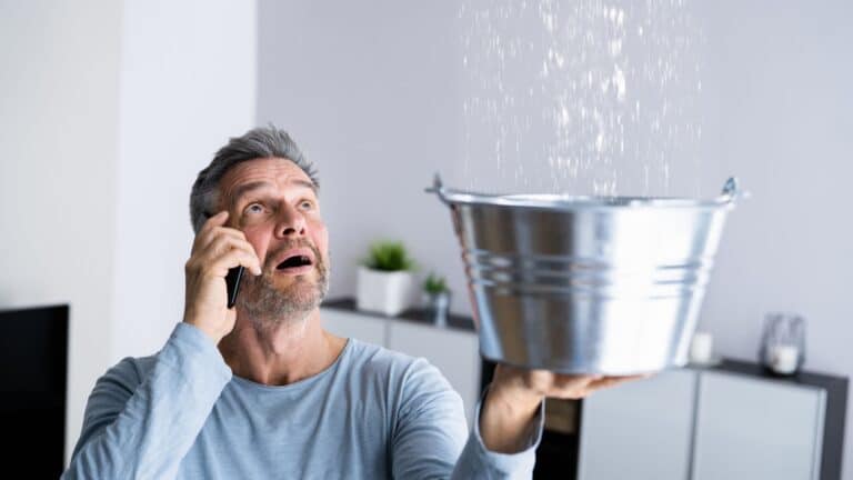 man holding a bucket to catch leaking water