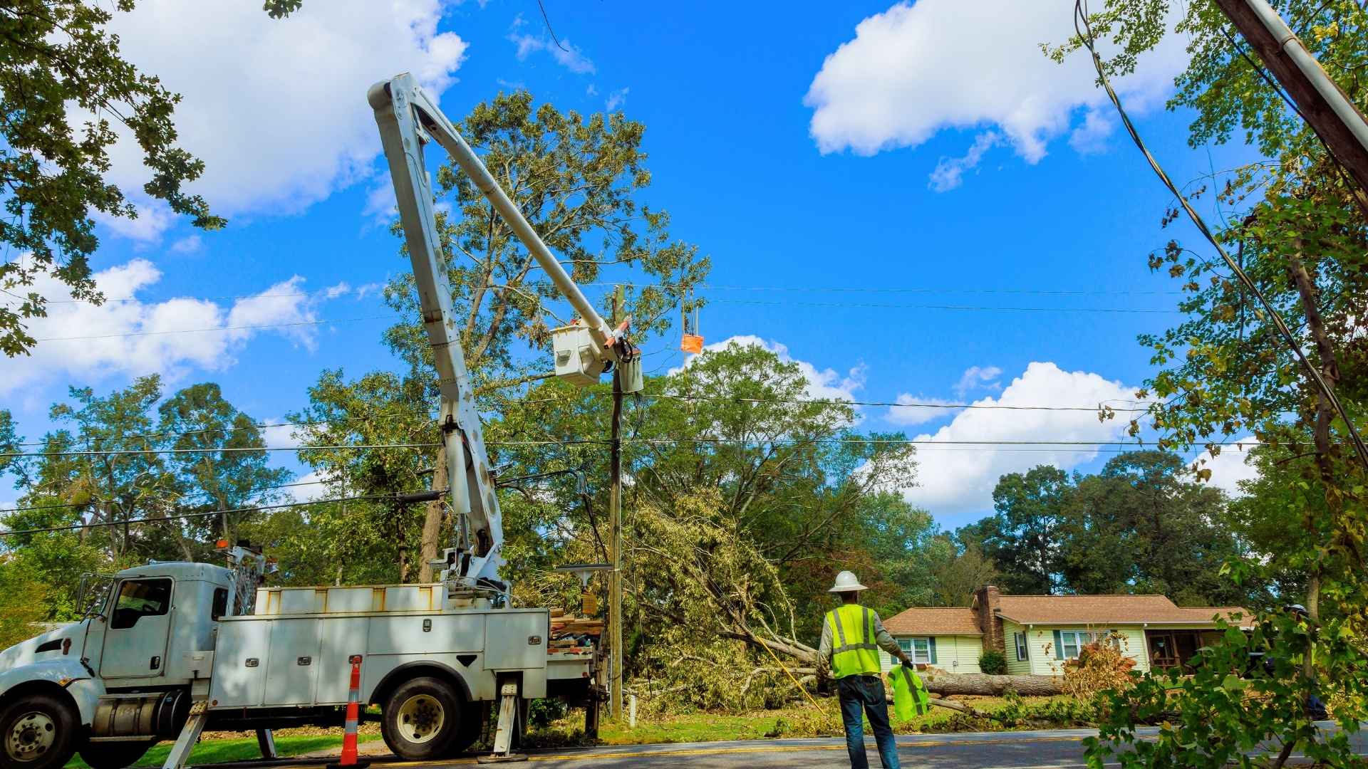 roof insurance claims in michigan Utility workers use a bucket truck to repair power lines after a fallen tree caused damage near a residential area.