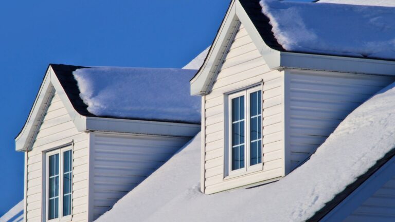 Two white dormer windows on a sloped roof covered in fresh, thick snow